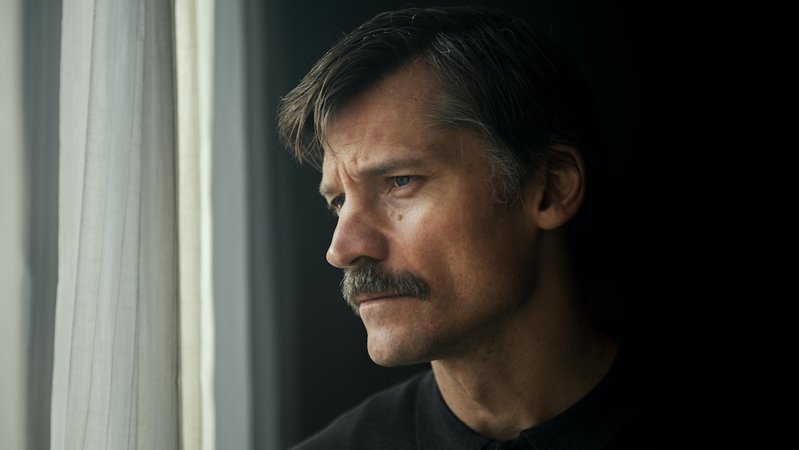 Mann mit Schnurrbart blickt sehr ernst aus dem Fenster:  Nikolaj Coster-Waldau als "Suicide Tourist” (Filmszene).