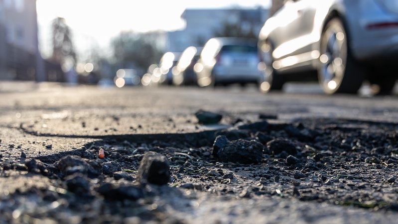 Ein Schlagloch auf einer Straße im Hintergrund parkende Autos (Symbolbild) | Bild: picture alliance / Andreas Gora|Lenny Karpe Ein Schlagloch auf einer Straße im Hintergrund parkende Autos (Symbolbild)