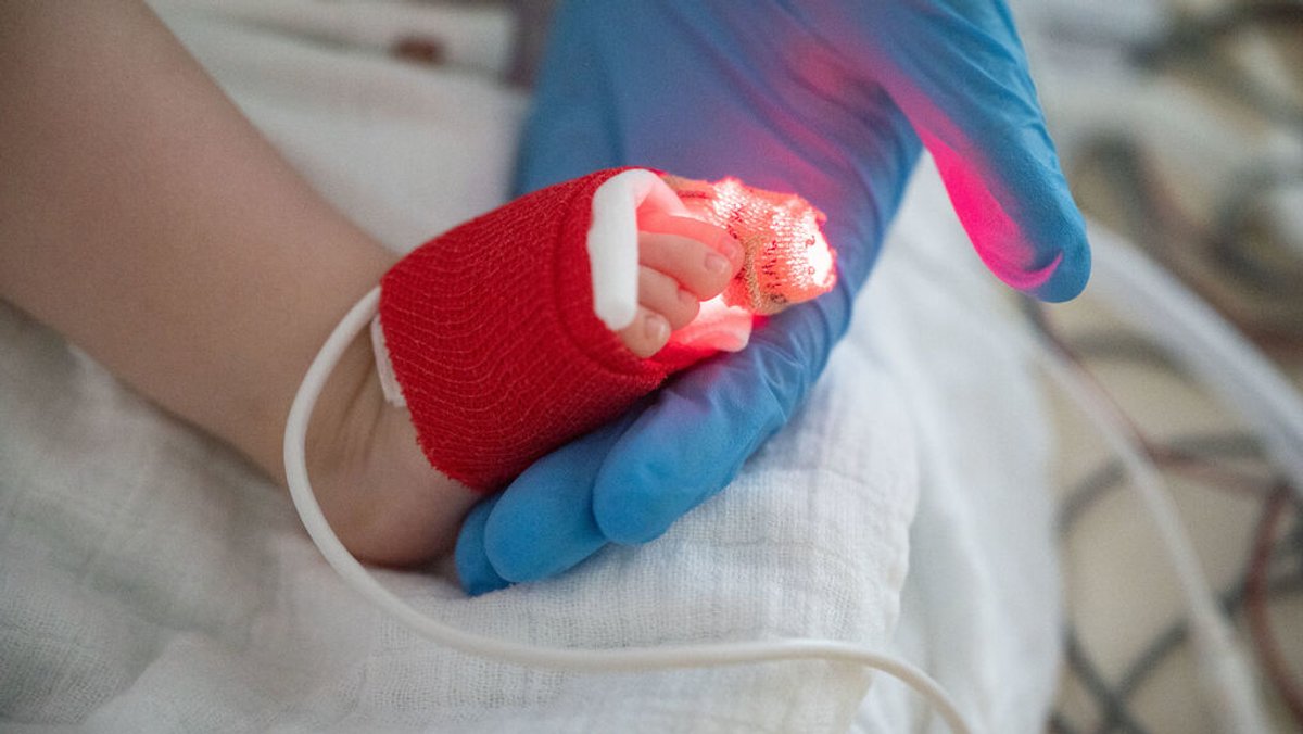 Eine Intensivpflegerin hält auf einer Kinder-Intensivstation den Fuß eines am Respiratorischen Synzytial-Virus (RS-Virus oder RSV) erkrankten Patienten, der beatmet wird, in der Hand. 