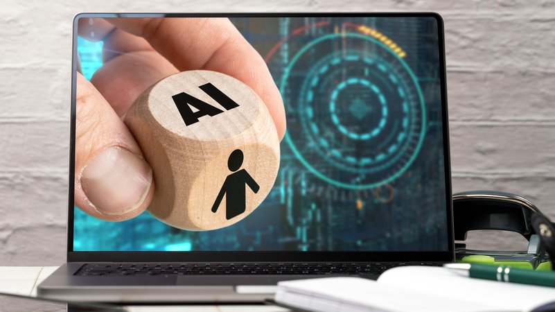 Eine Hand hält einen Würfel mit der Aufschrift AI vor einem Laptopbildschirm. | Bild: picture alliance / CHROMORANGE | MICHAEL BIHLMAYER Eine Hand hält einen Würfel mit der Aufschrift AI vor einem Laptopbildschirm.