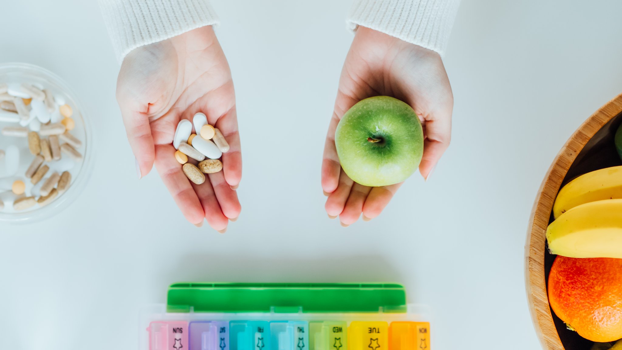 Zwei Hände - jeweils mit Tabletten und einem Apfel, Pillenschachtel und Obstteller