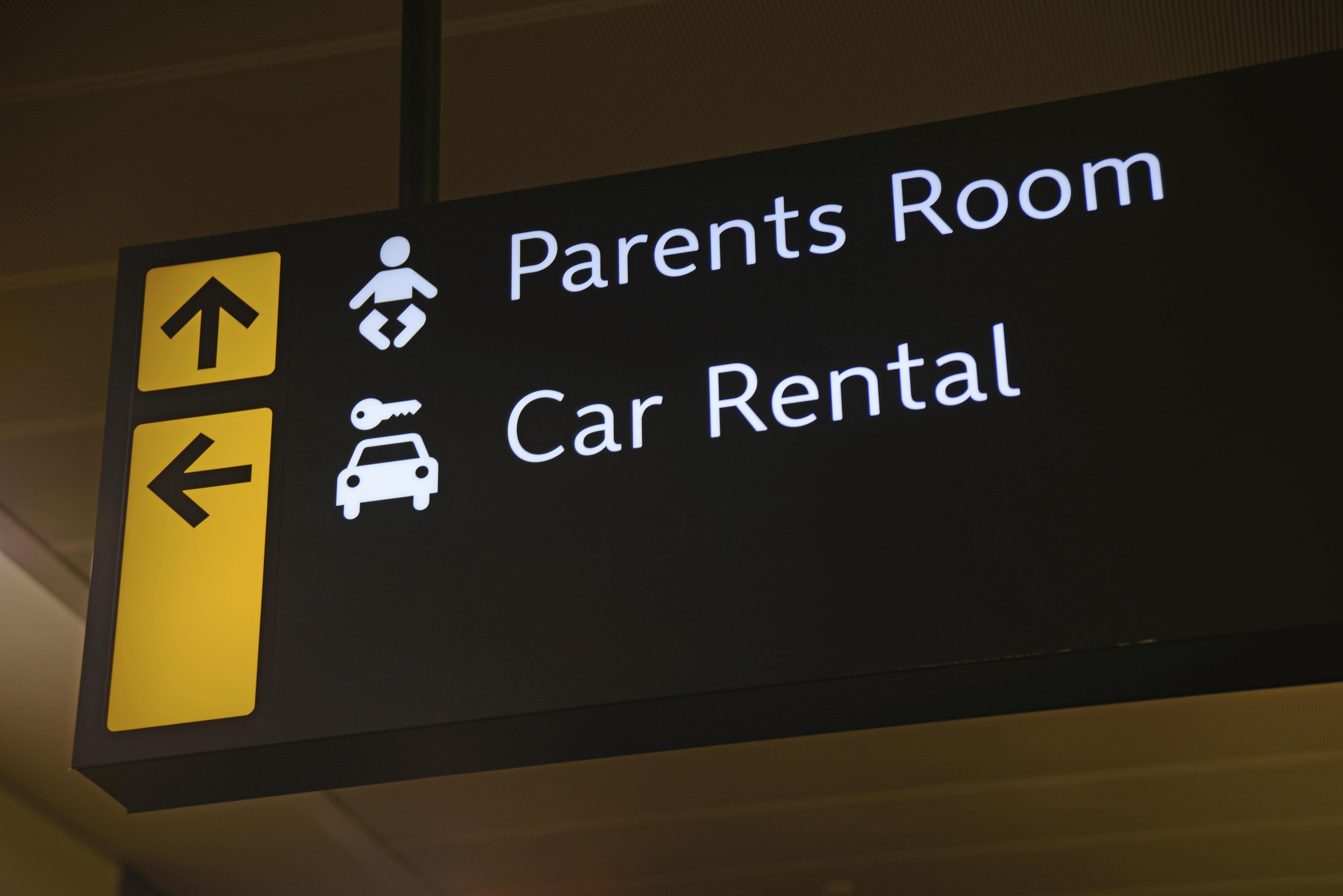 Schild an einem Flughafen weist Weg zu Autovermietern