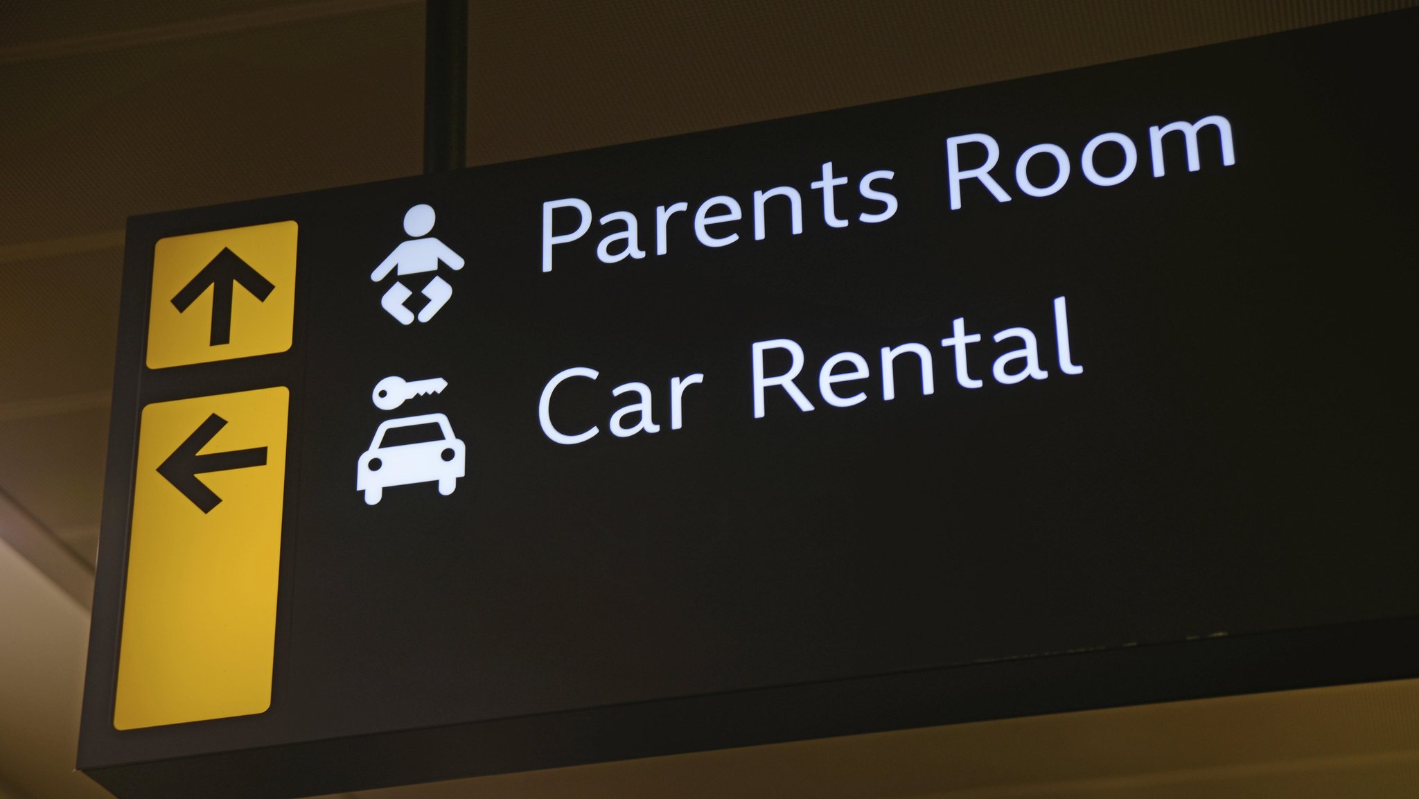 Schild an einem Flughafen weist Weg zu Autovermietern