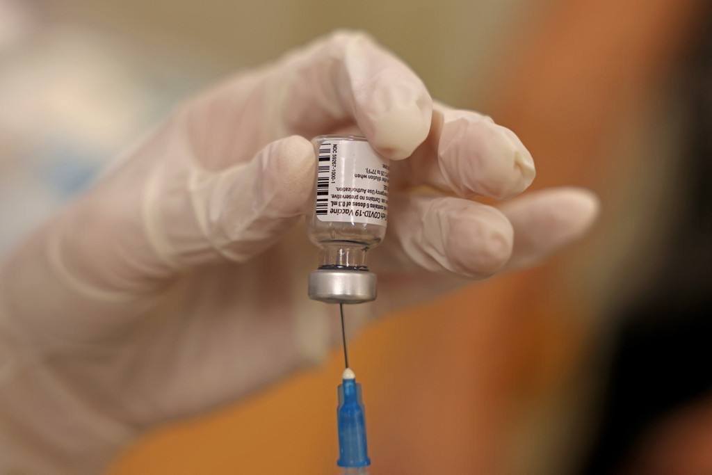 Ein Dosis Covid-19-Impfstoff wird auf eine Spritze aufgezogen; eine Hand mit Gummihandschuh hält das Fläschchen mit dem Impfstoff
