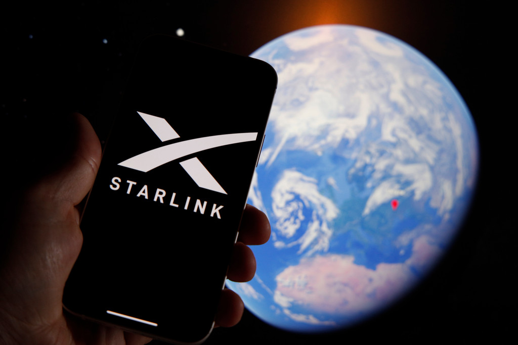 The Starlink logo is seen on a mobile device with an grahpic illustration of planet Earth