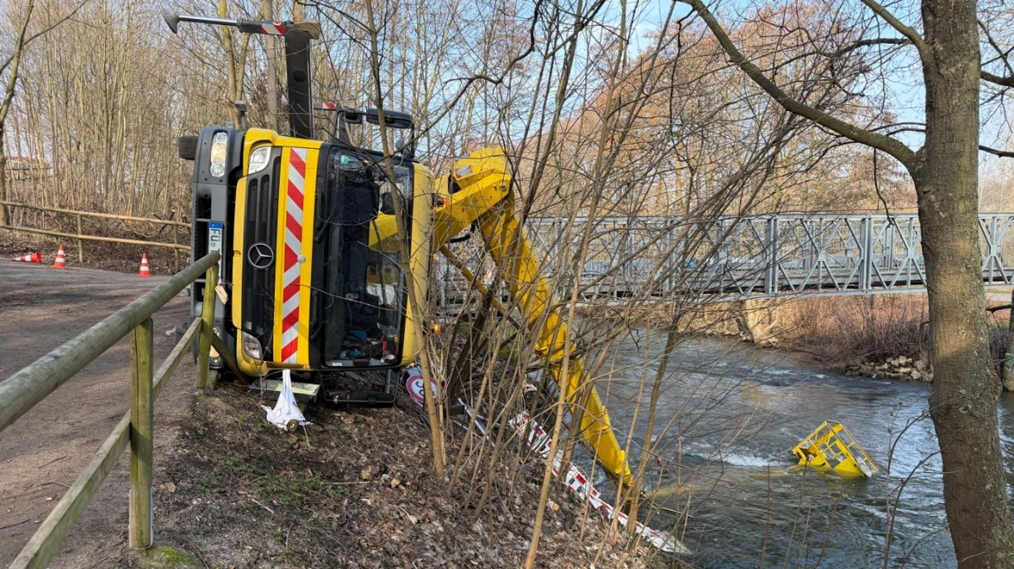 Ein Lastwagen ist mit seiner Arbeitsbühne umgekippt und liegt seitlich an einer Böschung.