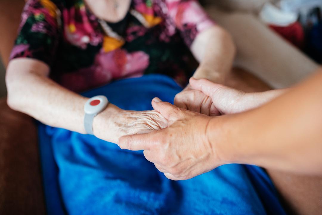 Eine jüngere Frau hält die Hände einer pflegebedürftigen älteren Frau