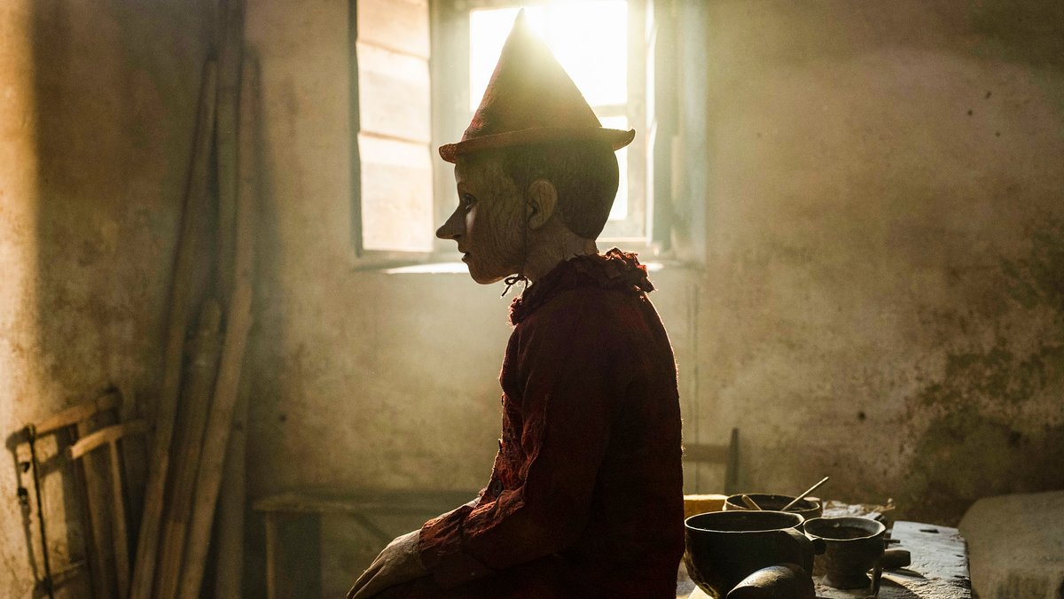 Ein Junge mit Hut sitzt im Gegenlicht vor einem Fenster in einem ärmlichen Raum: Szene aus "Pinocchio"