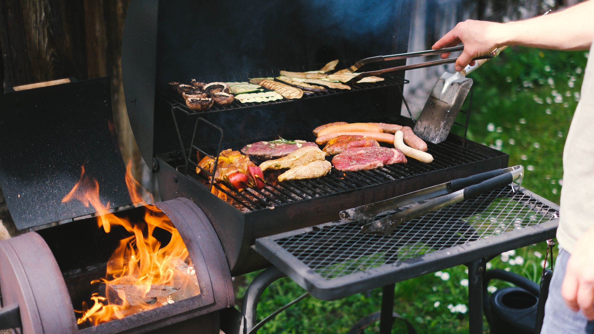 Ein Mann grillt Fleisch und Gemüse. 