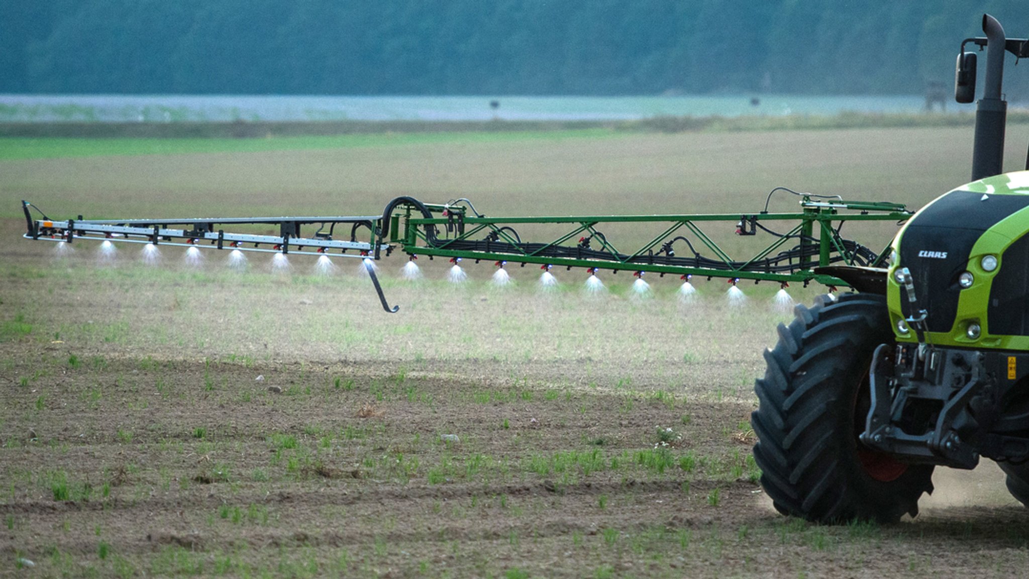 Ein Landwirt fährt abends mit einer Pestizid- und Düngerspritze über ein Feld.