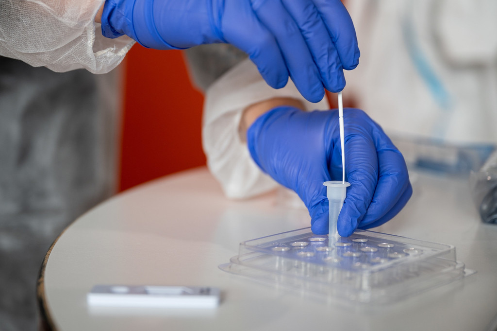 Hände in blauen Handschuhen führen Antigen-Test durch.