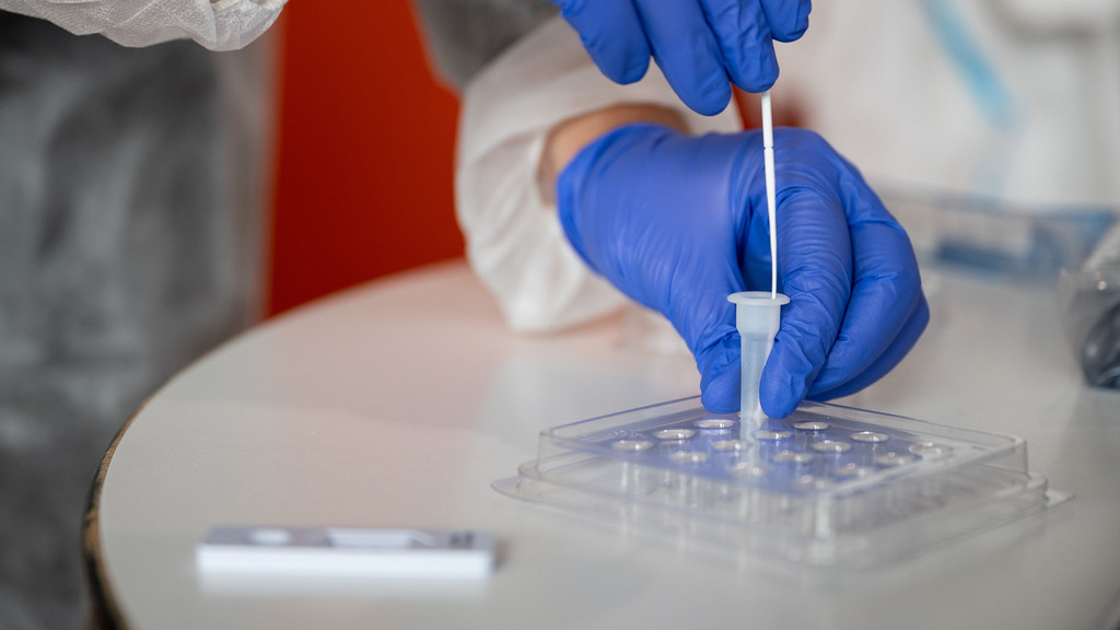 Hände in blauen Handschuhen führen Antigen-Test durch.