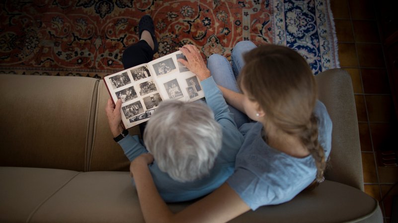 Eine junge Frau schaut mit einer alten Frau ein Fotoalbum durch.