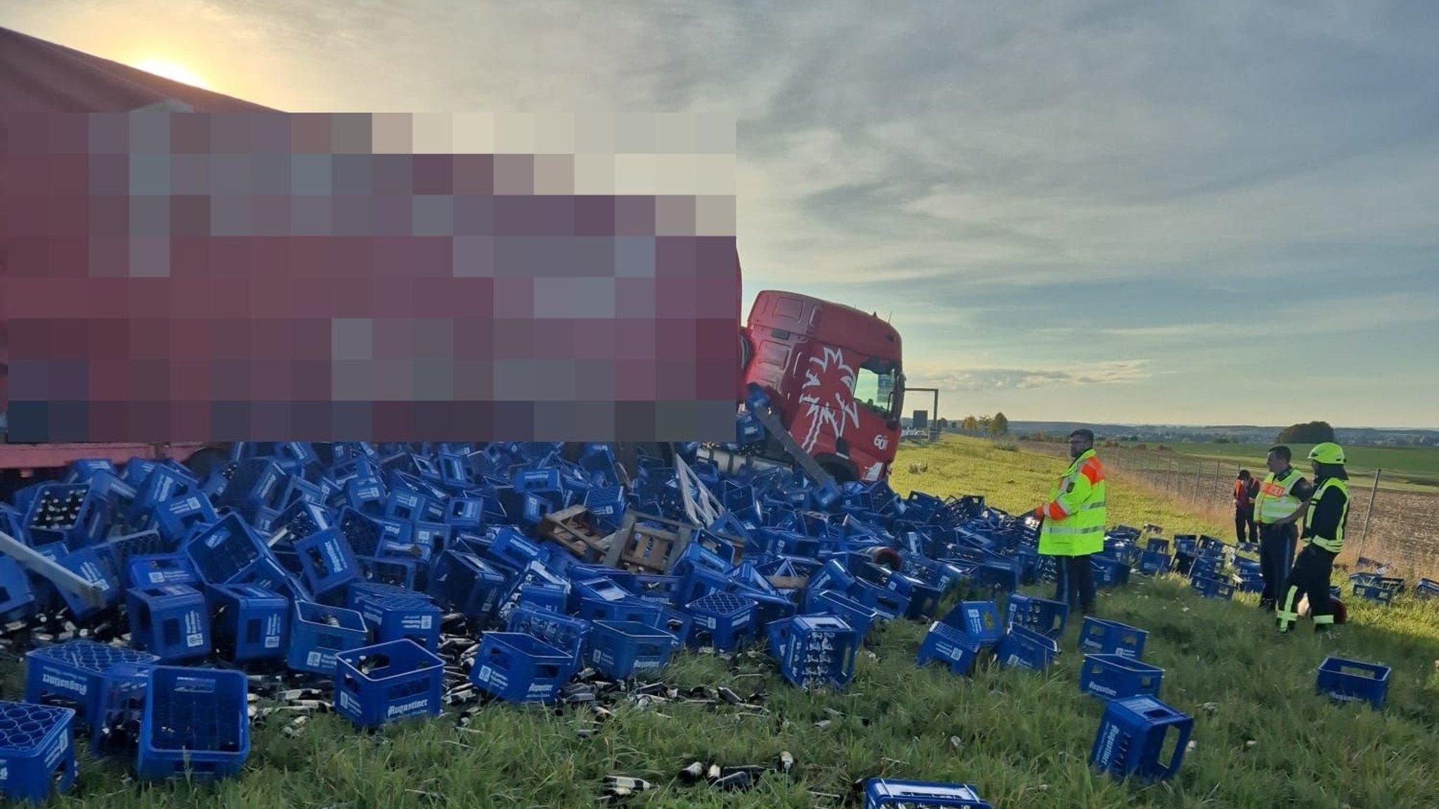 Ein LKW mit verschütteten Bierkästen. Daneben Feuerwehrleute auf eine Wiese.