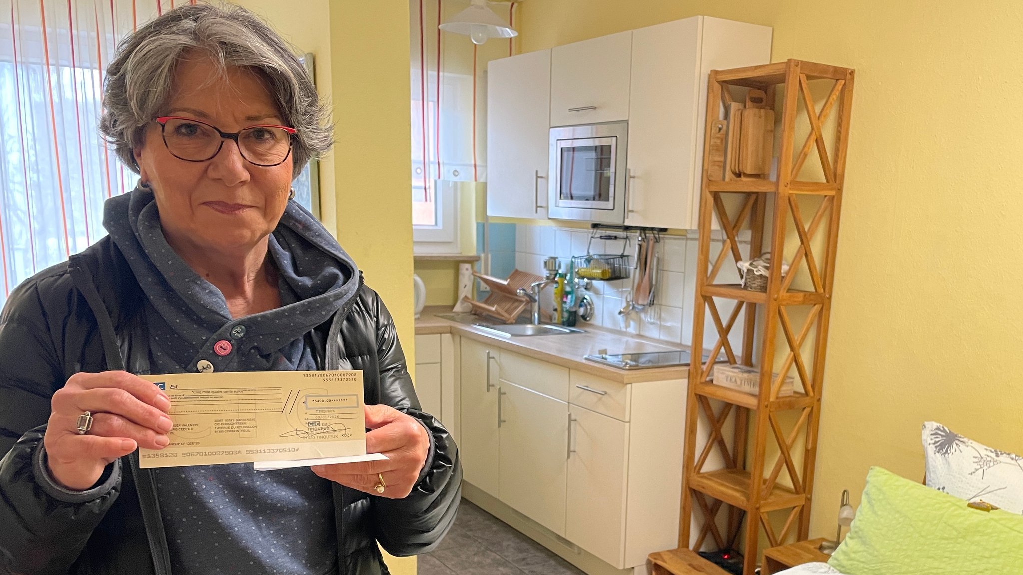 Eine Frau steht mit einem Scheck in der Hand in einer Ferienwohnung.