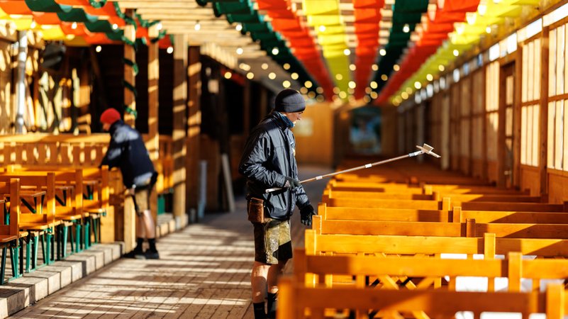 Mitarbeiter im Schützenfestzelt reinigen am Morgen vor der Öffnung vom Oktoberfestgelände die Bänke und Tische im Bierzelt. | Bild: dpa-Bildfunk/Matthias Balk Mitarbeiter im Schützenfestzelt reinigen am Morgen vor der Öffnung vom Oktoberfestgelände die Bänke und Tische im Bierzelt.