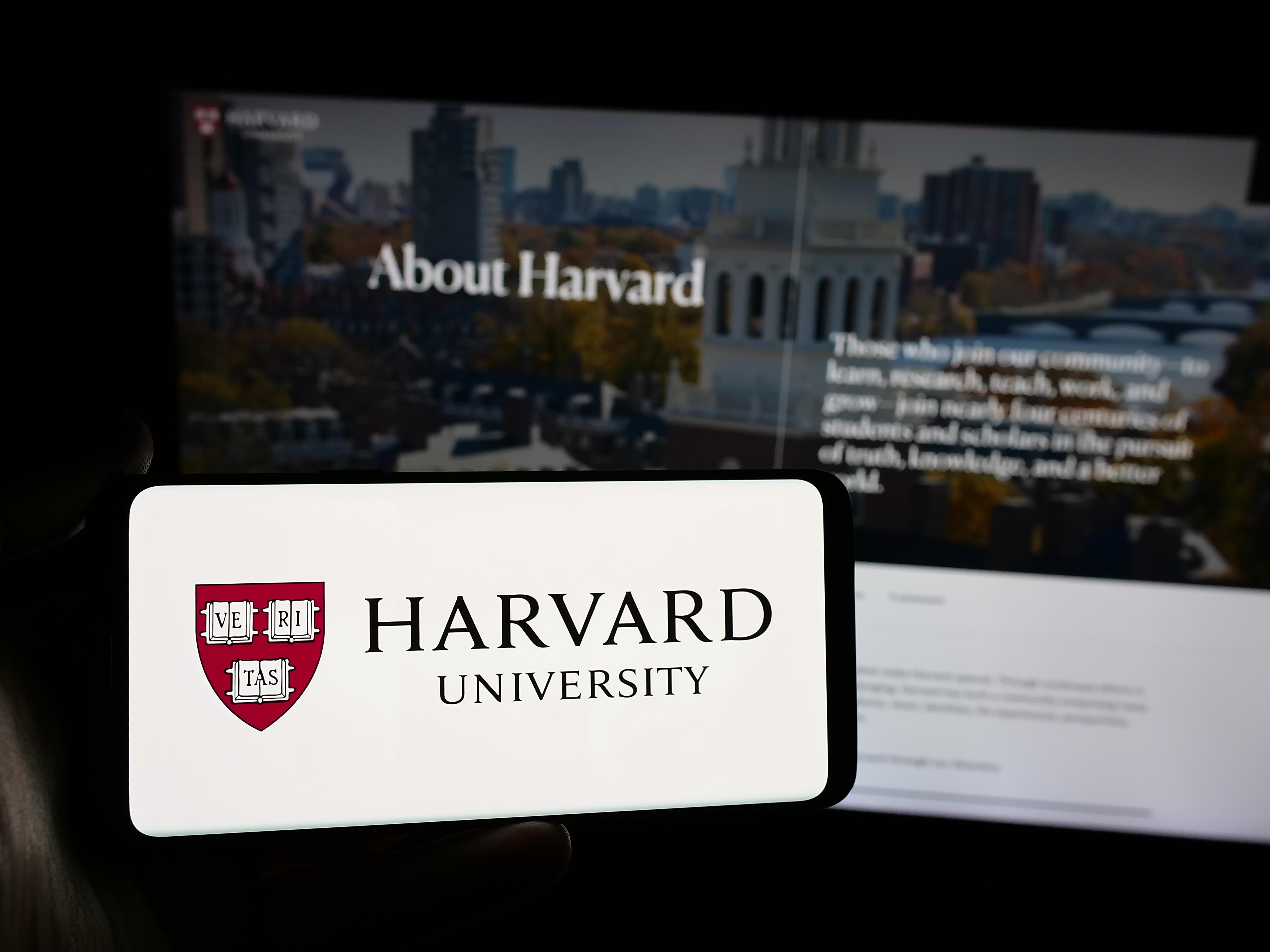 In dieser Fotoillustration hält eine Person ein Smartphone mit dem Logo der US-Forschungseinrichtung Harvard University vor einer Website der Harvard University.