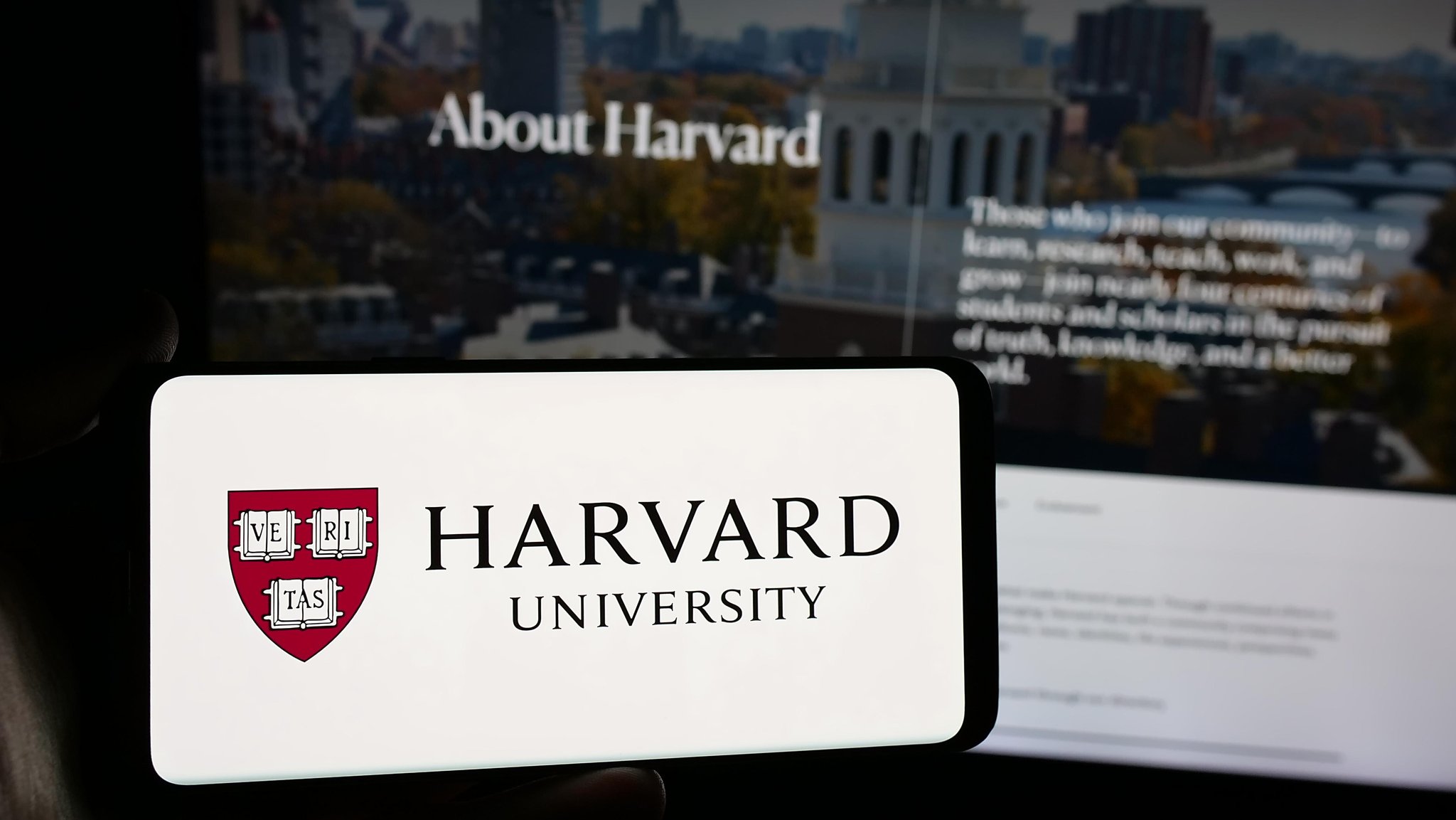 In dieser Fotoillustration hält eine Person ein Smartphone mit dem Logo der US-Forschungseinrichtung Harvard University vor einer Website der Harvard University. | Bild: picture alliance / Sipa USA | SOPA Images In dieser Fotoillustration hält eine Person ein Smartphone mit dem Logo der US-Forschungseinrichtung Harvard University vor einer Website der Harvard University.