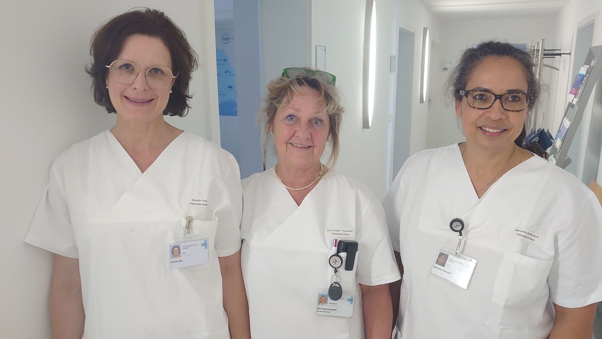 Drei Frauen im weißen Kittel stehen in dem Gang eines Krankenhauses.
