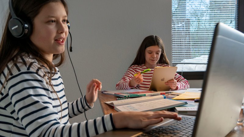 Zwei Mädchen sitzen an digitalen Endgeräten und lernen für die Schule