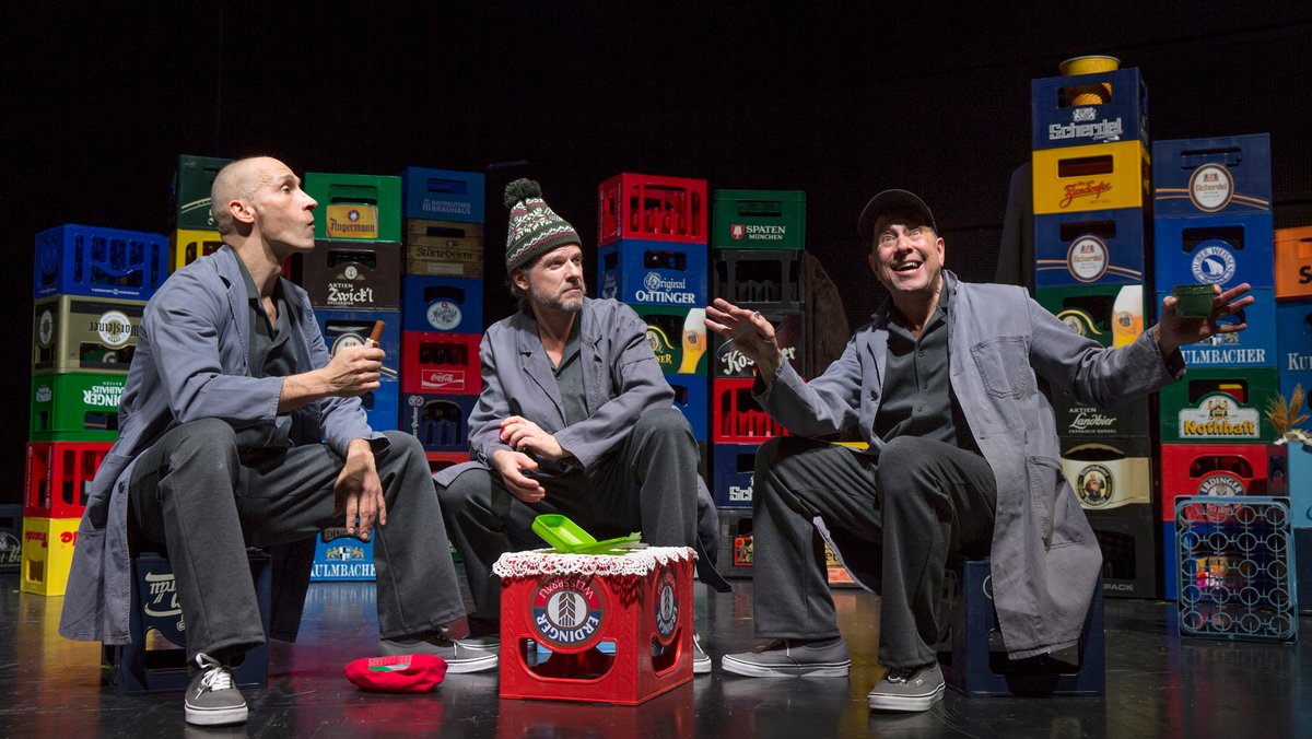 Drei Schauspieler sitzen auf Bierkästen auf einer Bühne.