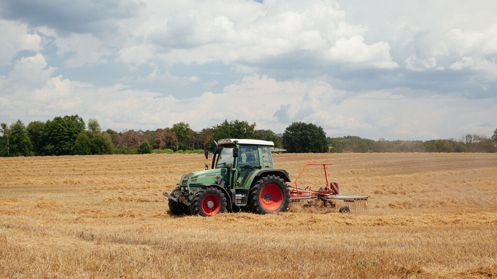 Ein Bauer der mit seinem Traktor das Heu auf seinem Feld wendet.