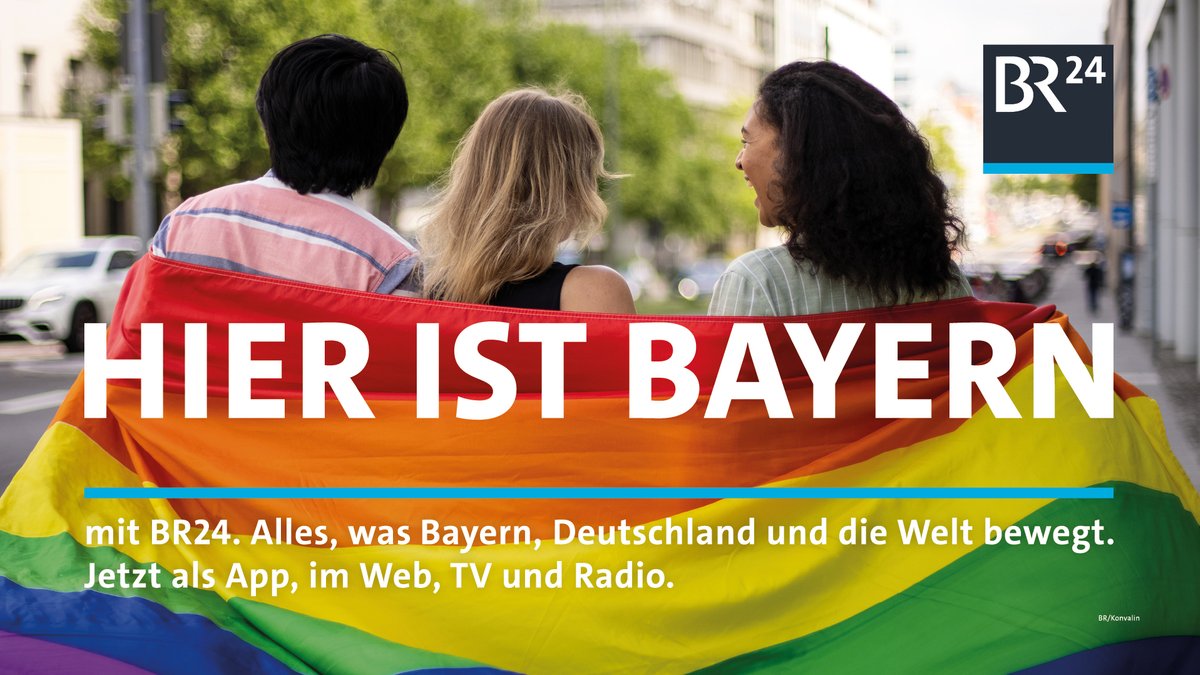 Hier ist Bayern: Drei junge Menschen in der LGBTIQ*-Fahne eingehüllt.