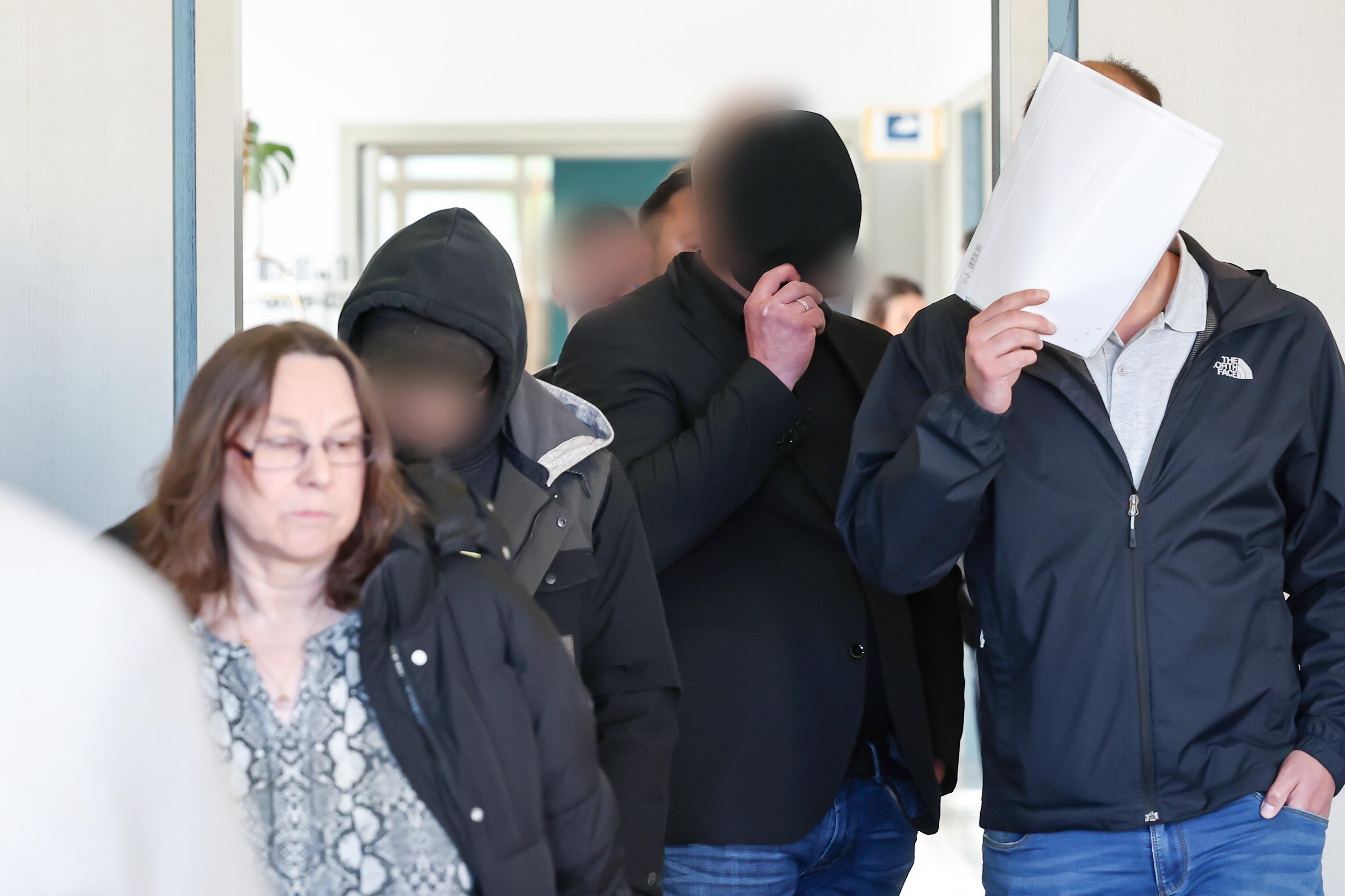 Männer kommen in einen Gerichtssaal. Daneben befindet sich ihre Verteidigerin. 