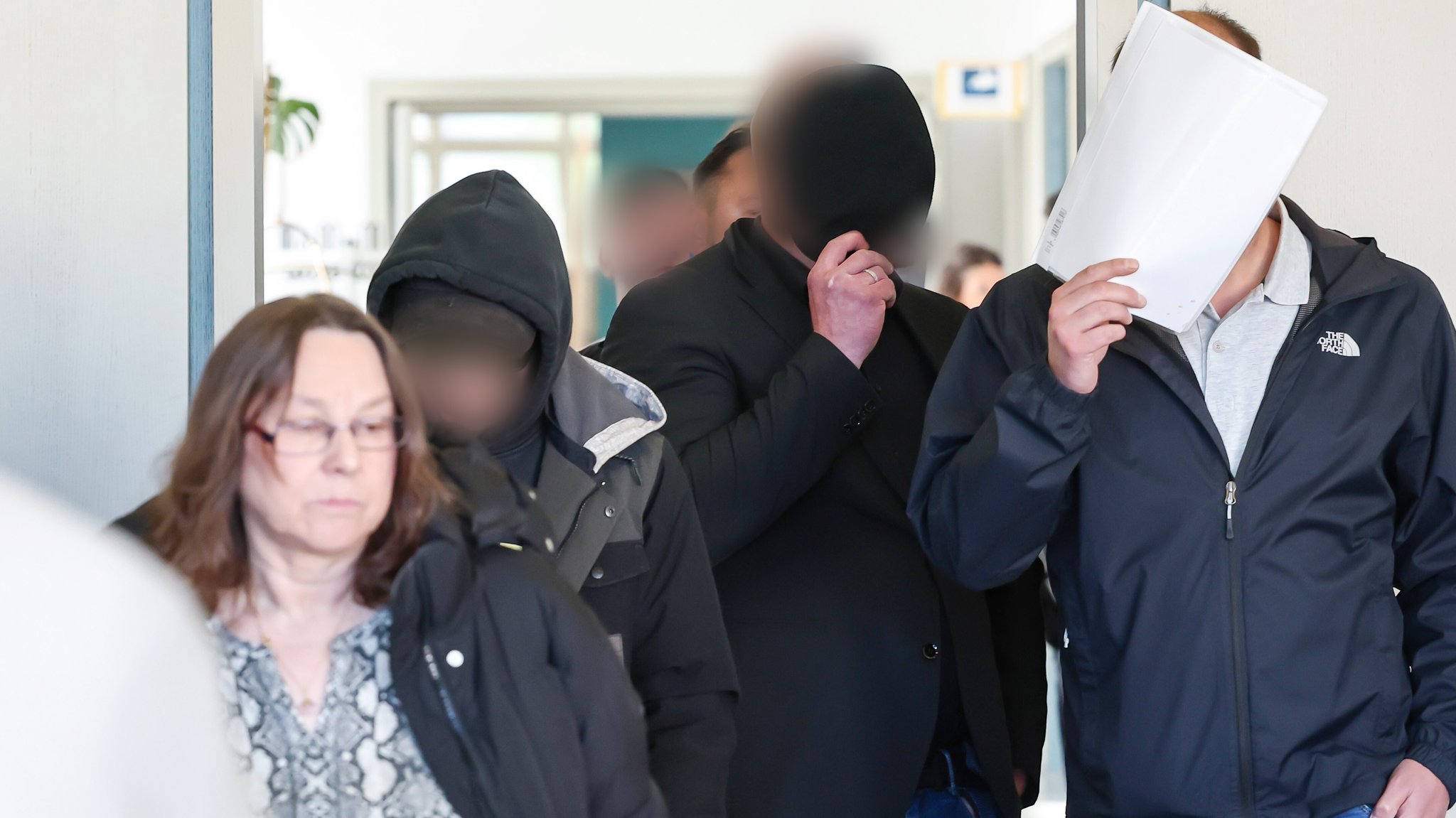Männer kommen in einen Gerichtssaal. Daneben befindet sich ihre Verteidigerin. 