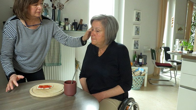 Barbara Windbergs (rechts) im Rollstuhl beim Frühstück. Ihre Assistentin hilft ihr. 