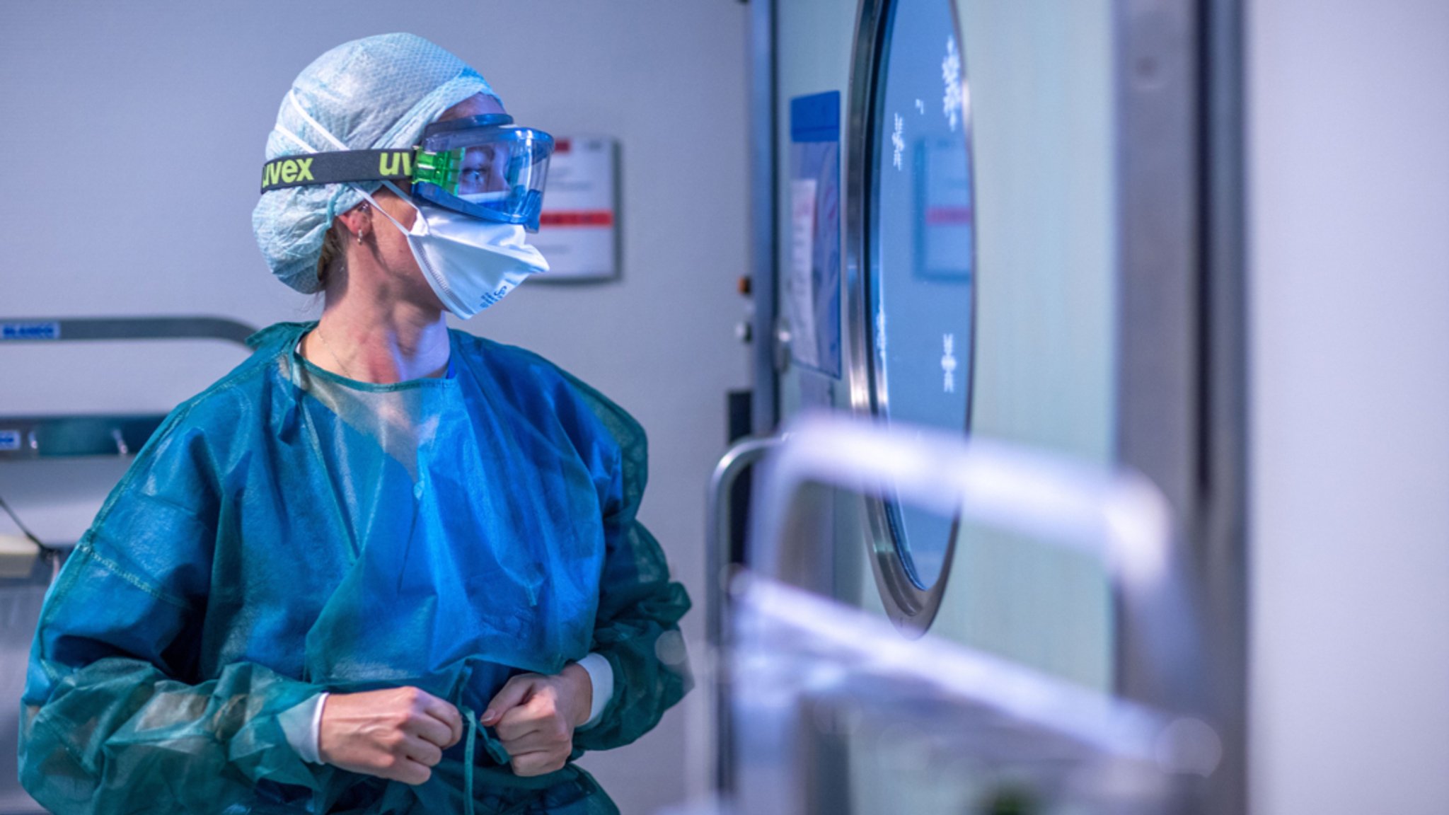 Eine Krankenpflegerin legt vor einem der Behandlungszimmer der Intensivstation ihre Schutzkleidung an. 