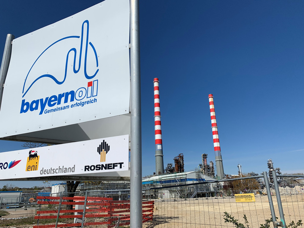 Blick auf die Bayernoil-Raffinerie in Vohburg mit zwei hohen, rot-weiß gestrichenen Schloten. Im Vordergrund das Firmenschild von Bayernoil.