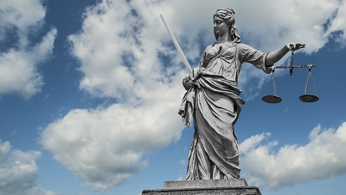 Statue einer Justizia mit Waage und Schwert vor einem Wolkenhimmel (Symbolbild)