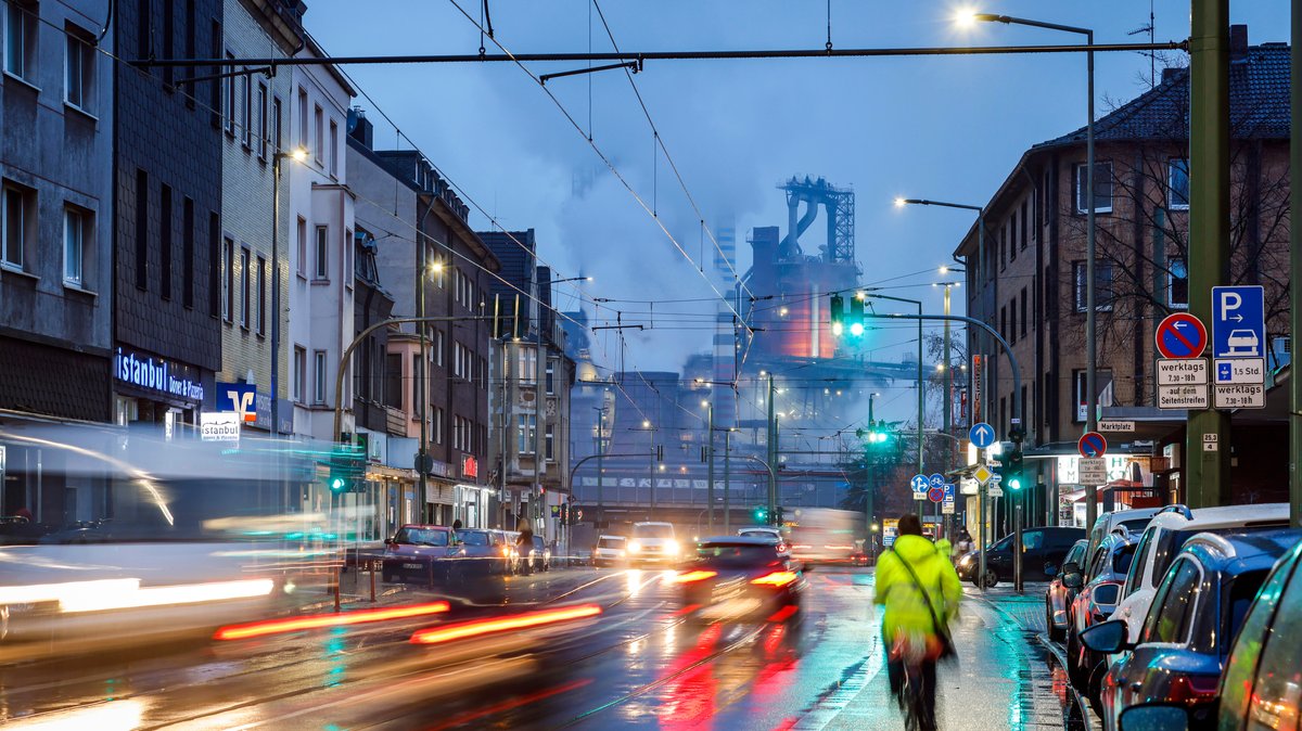 Stadtansicht mit dem ThyssenKrupp Huettenwerk in Duisburg-Bruckhausen, Fahrradfahrer im Vordergrund, Straßenverkehr, Feinstaub, Lungenkrebs.