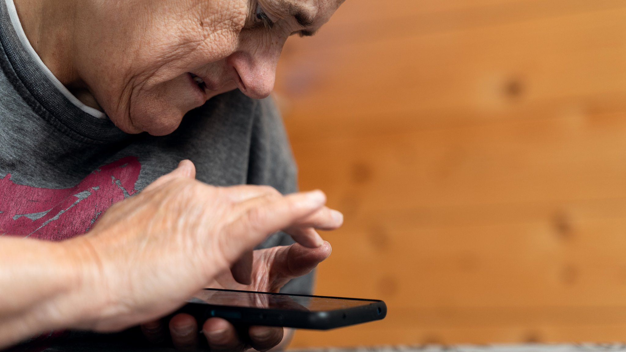 Seniorin mit Sehbehinderung und geistiger Behinderung nutzt ihr Smartphone zum Chatten, Streamen von Videos und Surfen im Internet (Symbolbild).