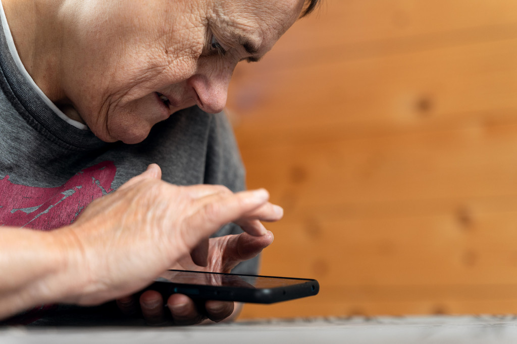 Seniorin mit Sehbehinderung und geistiger Behinderung nutzt ihr Smartphone zum Chatten, Streamen von Videos und Surfen im Internet (Symbolbild).