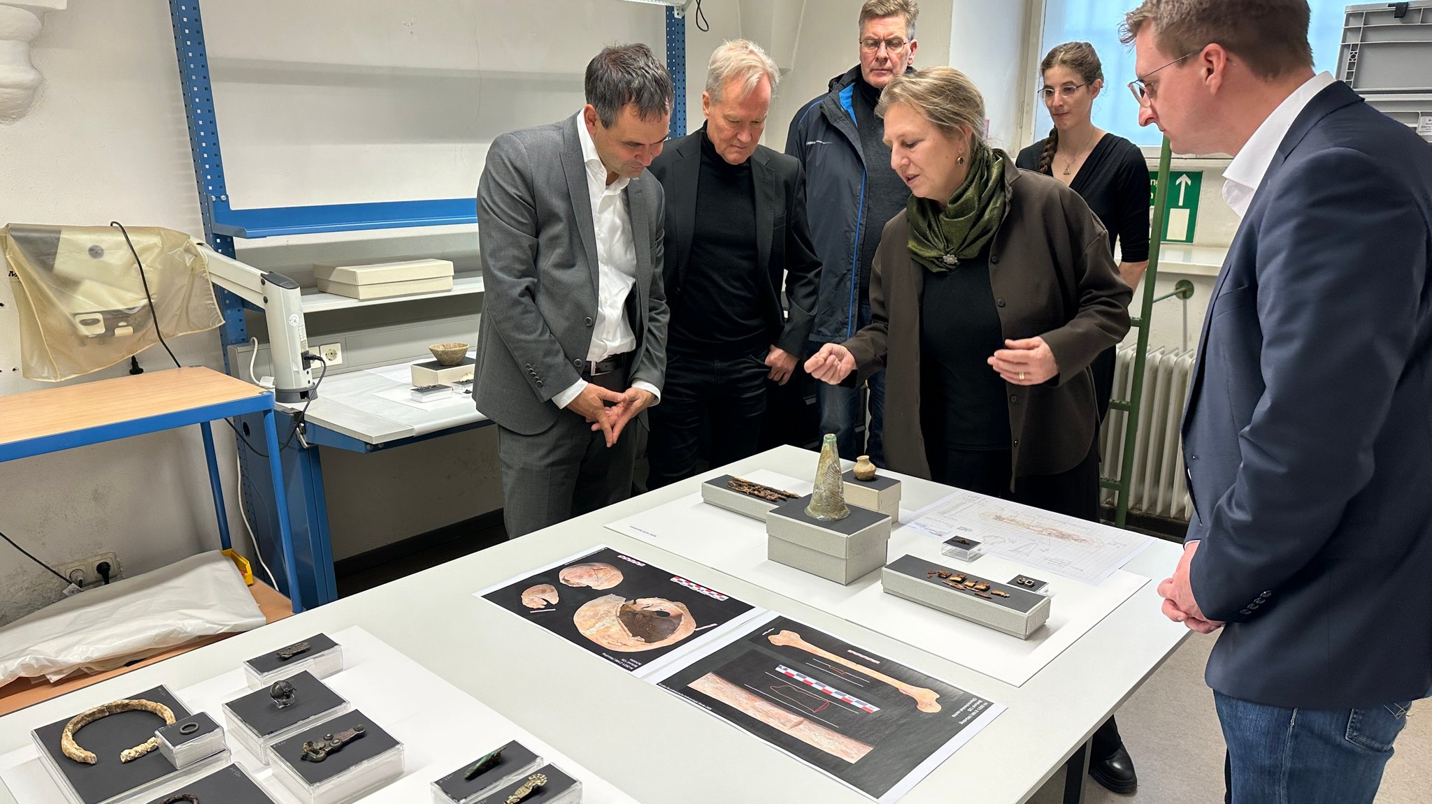 Sechs Personen stehen um einen Tisch mit restaurierten Grabbeigaben