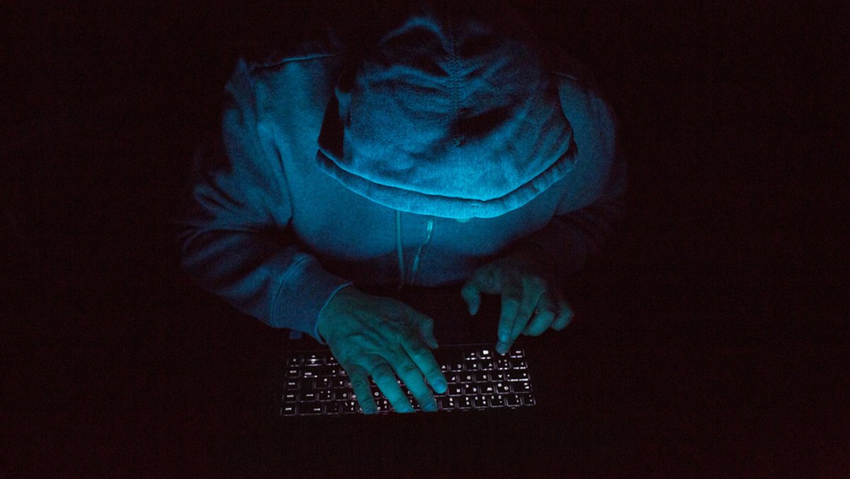 Ein Mann mit Kapuzenpullover arbeitet im Dunklen an einem Laptop.