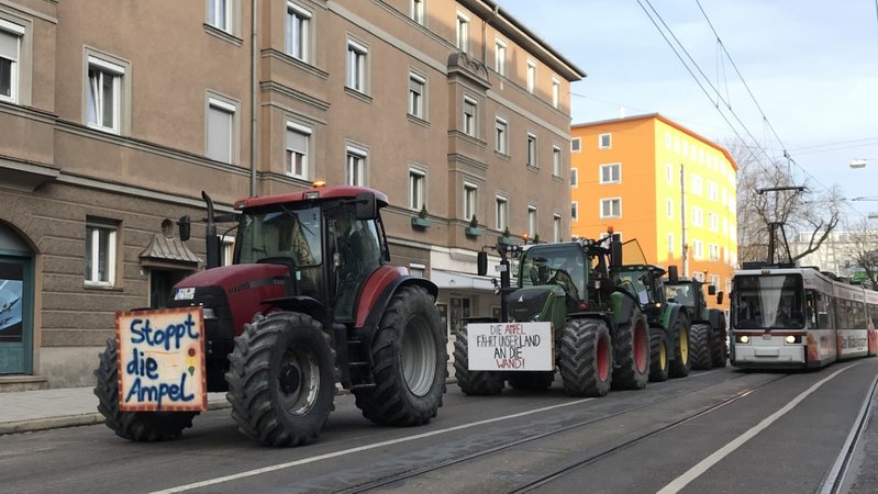 Mehrere Traktoren in der Augsburger Innenstadt neben einer Straßenbahn.