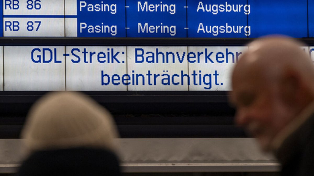 Bahnreisende stehen am Hauptbahnhof in München vor einer Anzeigetafel mit der Aufschrift "GDL-Streik: Bahnverkehr beeinträchtigt""