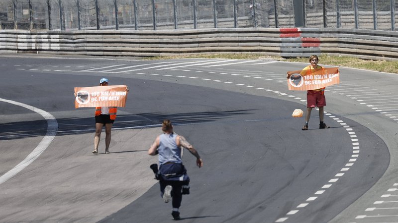Zwei Aktivisten stehen mit orangefarbenen Plakaten auf der Rennstrecke des Norisrings.