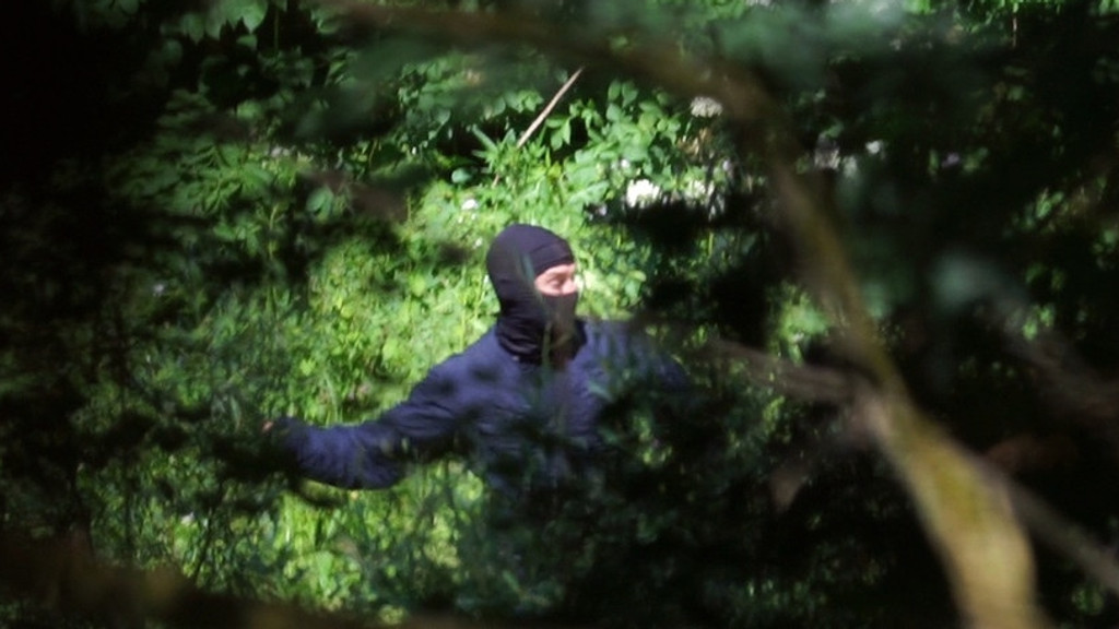 Ein Uniformierter an der kroatisch-bosnischen Grenze schlägt nach jemandem.