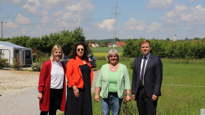 Bürgermeisterin, Anwohnerin und die Vorsitzenden von Zweckverband und Fremdenverkehrsverein stehen im Grünen vor einem hohen Strommasten.