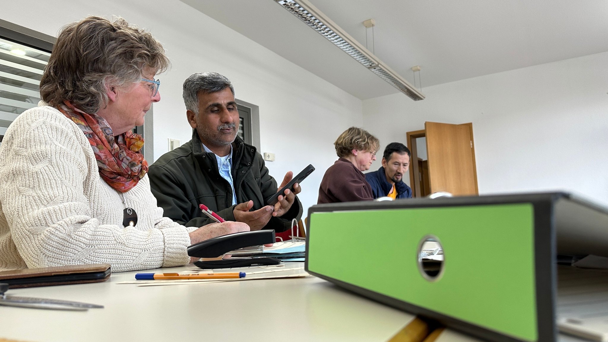 Die Ehrenamtliche Penny Edwards (links) hilft Abdul Molavizadeh (zweiter von links) aus Afghanistan, Ordnung in sein Dokumenten-Chaos zu bringen.