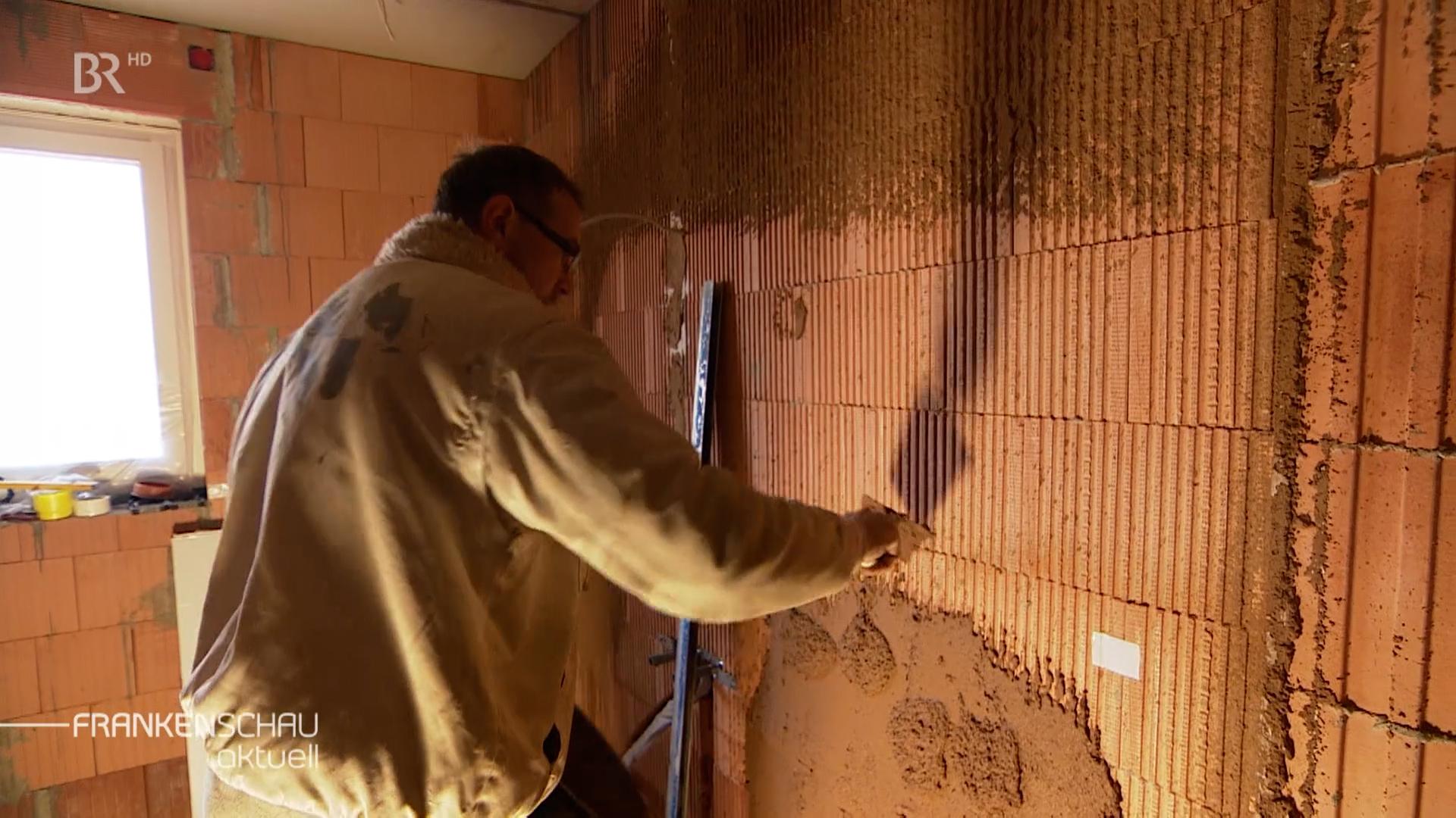Ein Handwerker verputzt eine Wand mit einem Gemisch aus gemahlenen Haselnussschalen.