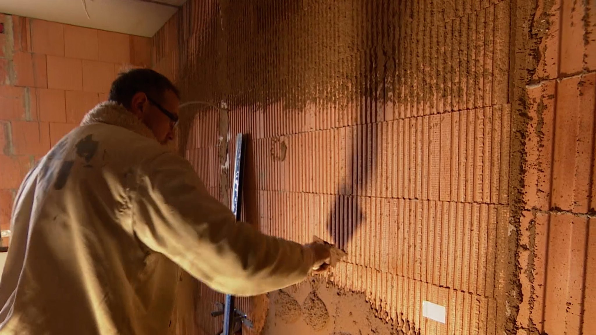 Ein Handwerker verputzt eine Wand mit einem Gemisch aus gemahlenen Haselnussschalen.