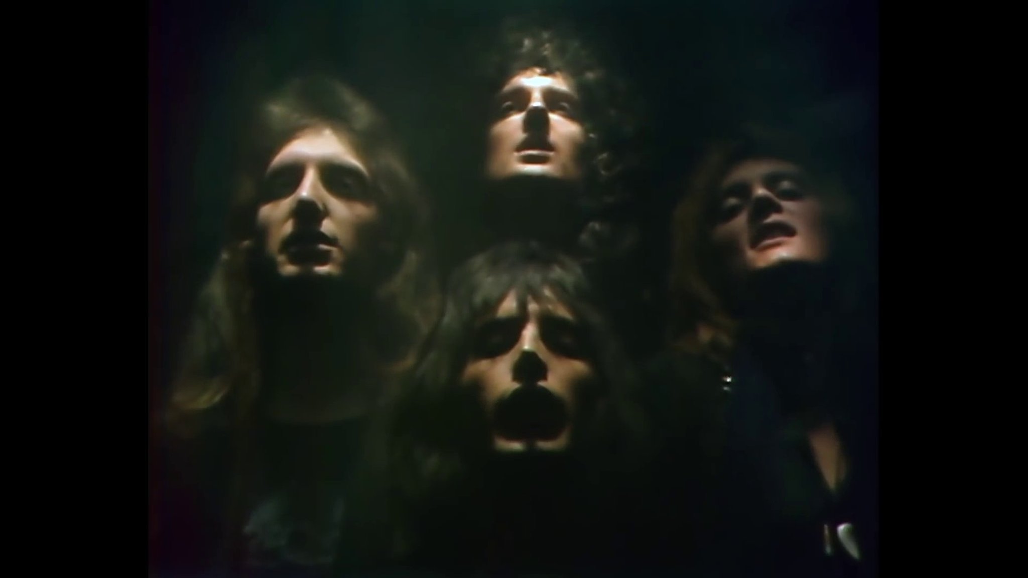 Die vier Köpfe der Bandmitglieder von Queen vor schwarzem Hintergrund