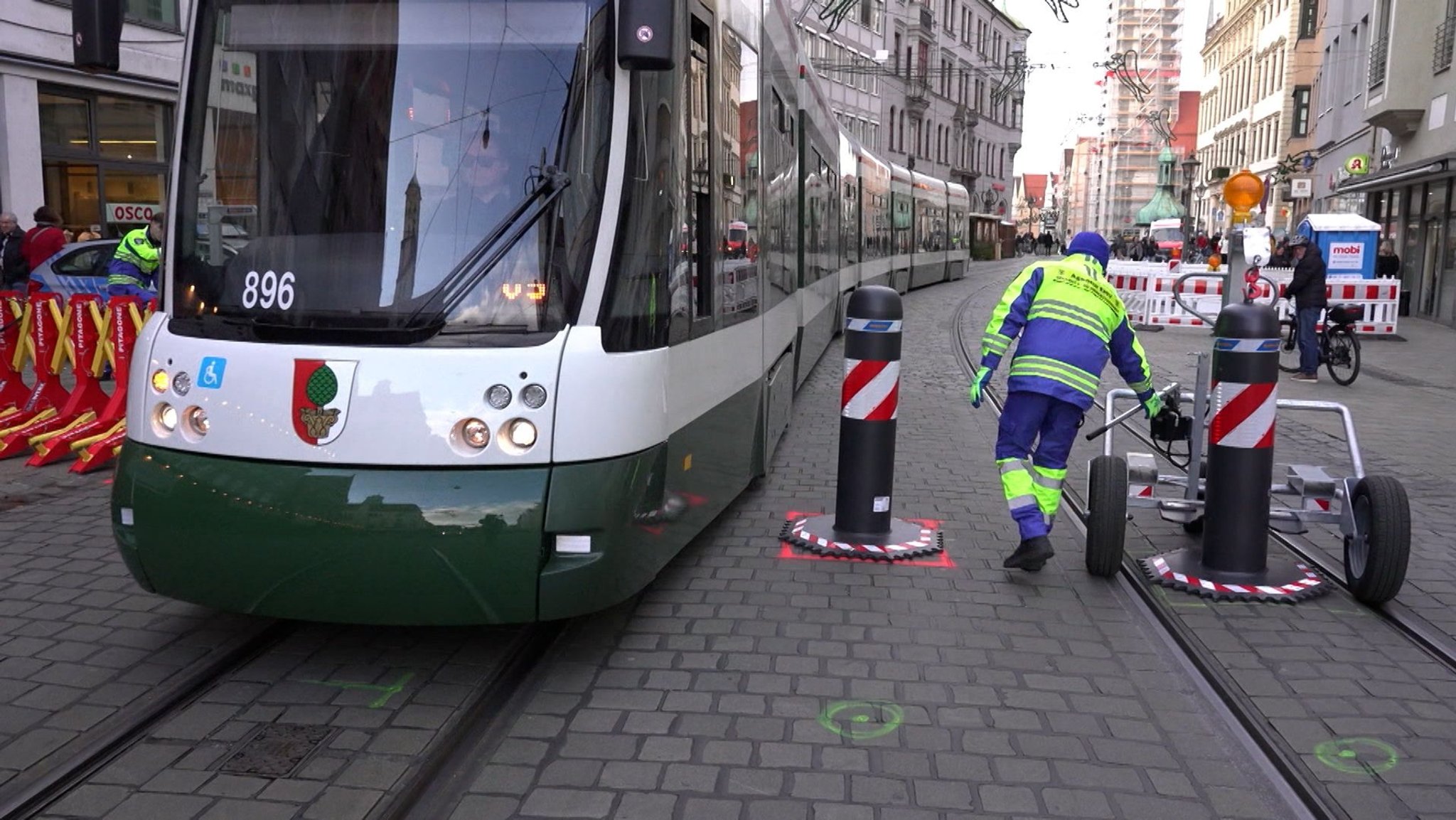 Eine Tram fährt in Augsburg an einem Mitarbeiter eines Sicherheitsdienstes vorbei, der sich um das Bewegen der Sicherheitspoller kümmert.