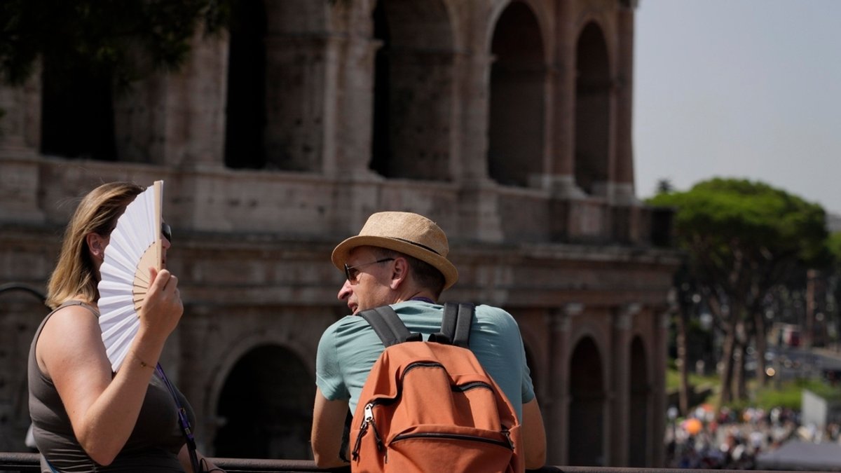 Touristen ruhen sich vor dem Kolosseum aus und fächern sich Luft zu