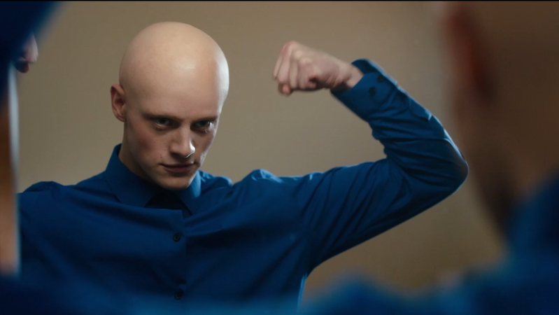 Ein junger Mann mit Glatze und blauem Hemd posiert vor einem Spiegel: Szene aus "Cluds"